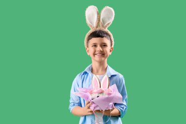 Yeşil arka planda Paskalya pastası olan tavşan kulağı takan şirin bir çocuk.