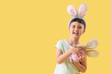 Paskalya hediyesi yumurtası ve sarı arka planda tavşan kulağı olan şirin bir çocuk.