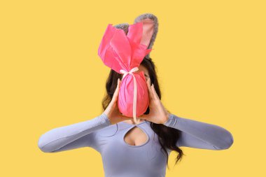 Tavşan kulaklı, sarı arka planda Paskalya hediyesi yumurtası olan genç bir kadın.