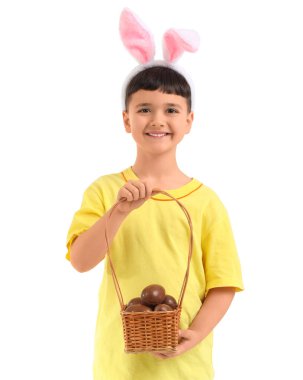 Beyaz arka planda Paskalya için çikolatalı yumurta sepeti tutan tavşan kulaklı şirin bir çocuk.