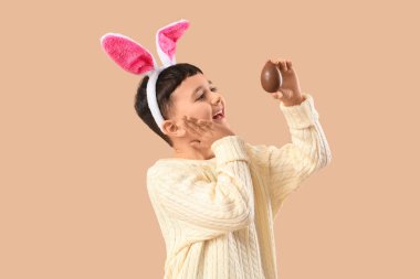 Bej arka planda Paskalya için çikolata yumurtası takan tavşan kulaklı şirin bir çocuk.