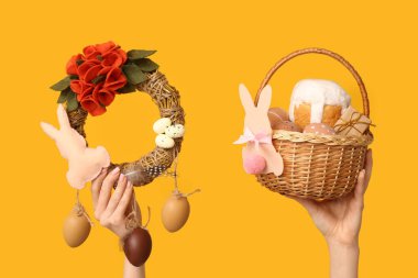 Paskalya bayramı çelengi ve sarı arka planda sepeti olan kadın eller.