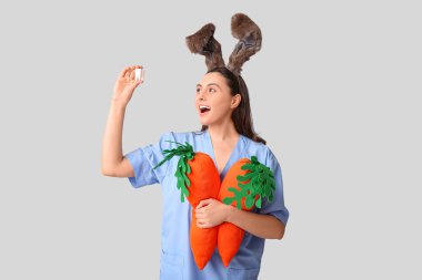 Tavşan kulaklı, oyuncak havuçlu ve gri arka planda plastik dişli kadın dişçi. Paskalya kutlaması