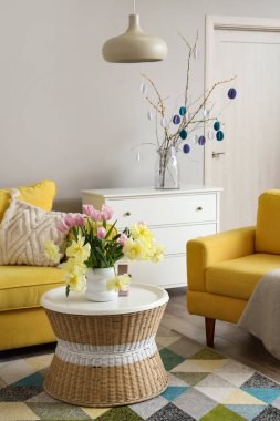 Paskalya kutlaması için dekore edilmiş oturma odasındaki masada duran güzel laleli ve oyuncak tavşanlı vazo.