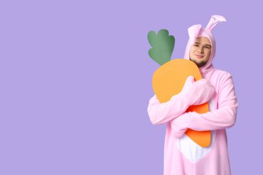 Leylak kaplamalı kağıt havuçlu tavşan kostümlü genç adam. Paskalya kutlaması