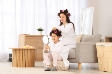 Küçük kızı evde kıvırcık saçlı genç Asyalı kadın.