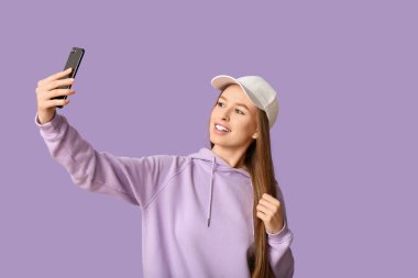 Beyaz şapkalı güzel bir kadın leylak arkaplanda selfie çekiyor.