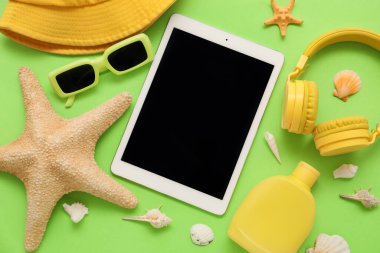 Tablet ve plaj aksesuarları, güneş kremi ve yeşil arka planda güneş gözlüğü. Yakın çekim.