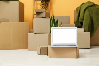 Odada turuncu duvarın yanındaki kutuları taşıyan boş bir dizüstü bilgisayar.