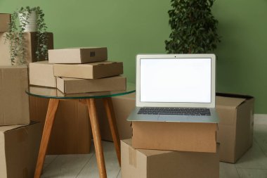 Boş dizüstü bilgisayar, taşınan kutular, masa ve yeşil duvarın yanındaki bitkiler.