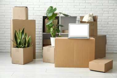 Boş dizüstü bilgisayar, bitkiler ve beyaz tuğla duvarın yanındaki kutular.