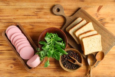 Lezzetli kaynamış sosis, ekmek, karabiber ve kahverengi ahşap arka planda fesleğen dilimleri olan tahtalar.