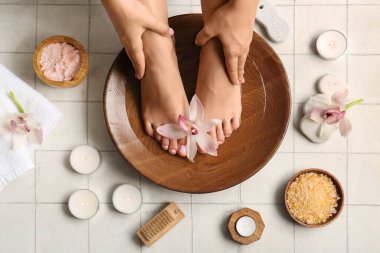 Orkide çiçekleri, deniz tuzu ve beyaz fayanslı mumlarla spa prosedürü için kasedeki kadın bacakları.