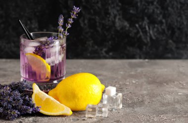 Bir bardak taze lavantalı limonata, çiçekler ve limonlar gri masada.
