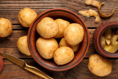 Tahta arka planda çiğ patates ve bıçaklı kaseler.