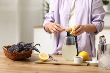 Mutfaktaki masada lavantalı limonata hazırlamak için limon sıkan genç kadın.