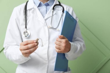 Renk duvarının yanında işitme cihazı ve panosu olan kadın doktor.