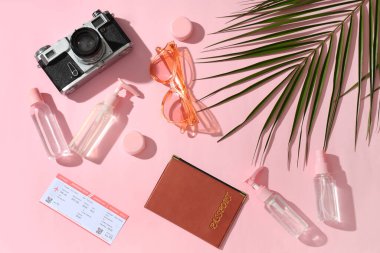 Seyahat kozmetik ürünleri, güneş gözlükleri, fotoğraf makinesi ve pembe arka planda palmiye yaprağı bileşimi