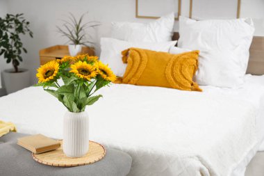 Yatak odasının içinde rahat bir yatak odası ve başucunda güzel ayçiçekleri var.