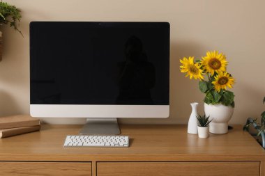 Modern bilgisayarı ve bej duvarın yanında ayçiçekleri olan güzel bir iş yeri.