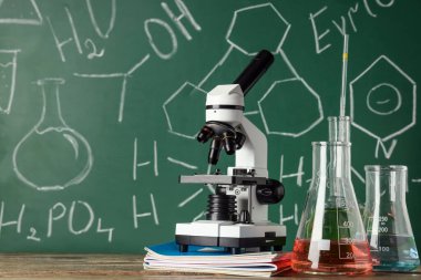 Modern mikroskop ve mataralar ahşap masada, kimyasal formüllerle birlikte.