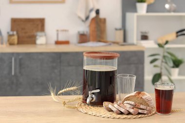 Kavanoz dolusu lezzetli kvass, bardaklar, ekmek dilimleri ve mutfaktaki masada dikenler.