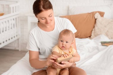 Kitaplı anne ve küçük bebeği evde yatağında oturuyor.