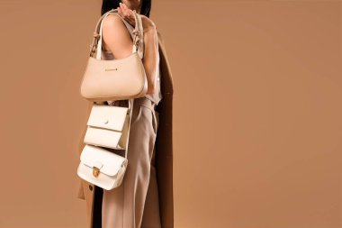 Bej arka planda farklı tarz çantaları olan güzel bir genç kadın, yakın plan.