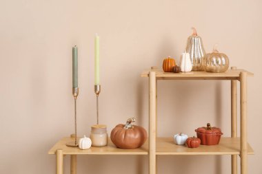 Balkabağı şeklinde mumlar ve bej duvarın yanında süslemeler olan raf ünitesi