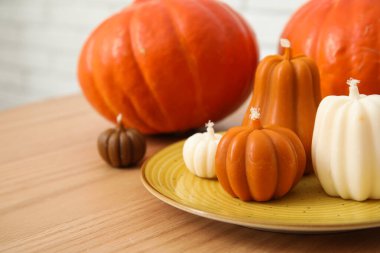 Beyaz tuğla duvarın yanında balkabağı şeklinde mumlarla kahve masası. Yakın çekim.