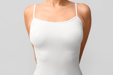 Gri arka planda güzel göğüsleri olan kolsuz tişörtlü genç bir kadın, yakın plan.