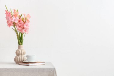 Üzerinde bir buket güzel gladiolus çiçeği, kitap ve kahve olan bir vazo beyaz arka planda.
