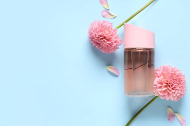 Bir şişe parfüm, yıldız çiçekleri ve mavi arka planda yapraklar.