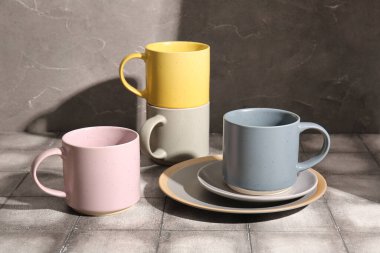 Gri duvarın yanındaki gri masada farklı seramik bardaklar ve plakalar.