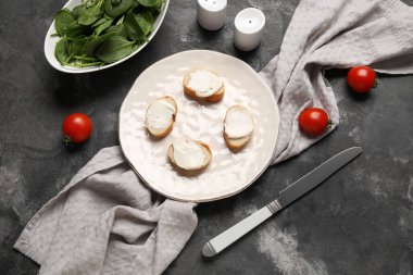 İşlenmiş peynirli lezzetli bruschetta tabağı, ıspanak yaprakları ve siyah arka planda taze domatesler.