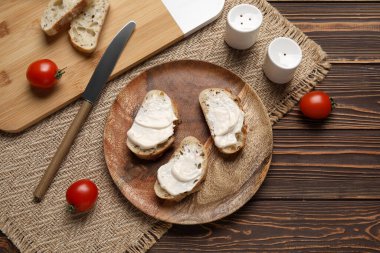 İşlenmiş peynirli lezzetli bruschetta tabağı ve ahşap zemin üzerinde taze domatesler.