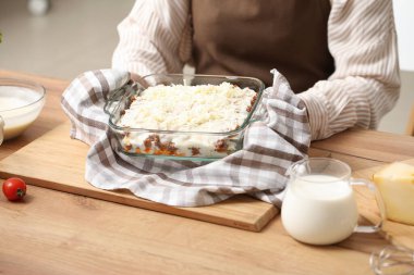 Güzel, olgun bir kadın mutfakta çiğ lazanya ile fırın tabağı tutuyor.