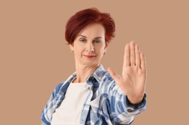 Olgun bir kadın bej arka planda DUR hareketi gösteriyor. Kural kavramı