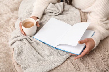 Evinde battaniye ve kahve fincanı okuyan genç bir kadın var.