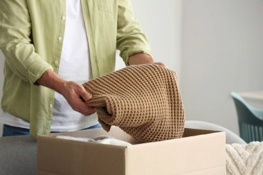 Yetişkin bir adam evinde giysileriyle birlikte kutuları açıyor.