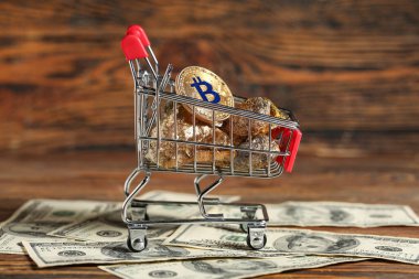 Tahta arka planda altın külçeli alışveriş arabası, bitcoin ve dolar banknotları.