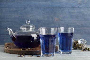 Bardaklar ve çaydanlıklar mavi ahşap arka planda bezelye çiçeği çayı