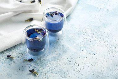 Cups of butterfly pea flower tea on blue grunge background with space for text clipart