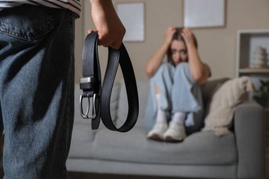 Kemerli bir adam ve korkmuş karısı evde, yakın plan. Aile içi şiddet kavramı