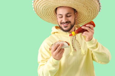 Yeşil arka planda lezzetli taco ve soslu genç Meksikalı adam.