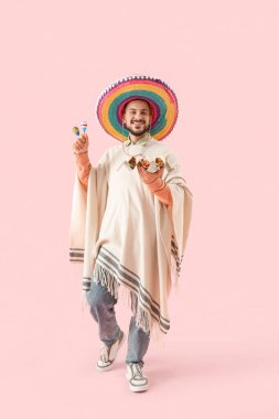 Pembe arka planda lezzetli tacoları ve marakaları olan genç Meksikalı adam.