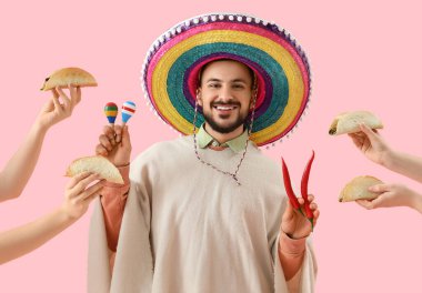 Marakas, kırmızı biber ve elleri pembe arka planda lezzetli taco tutan genç Meksikalı adam.