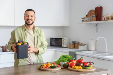 Mutfakta yemek pişirirken gübre kutusu ve sebze artıklarıyla gezen genç adam.