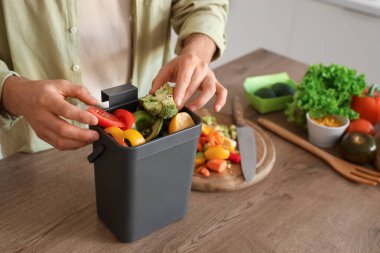 Mutfakta yemek pişirirken gübre kutusu ve sebze artıklarıyla gezen genç adam.