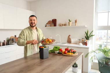 Mutfakta yemek pişirirken gübre kutusu ve sebze artıklarıyla gezen genç adam.